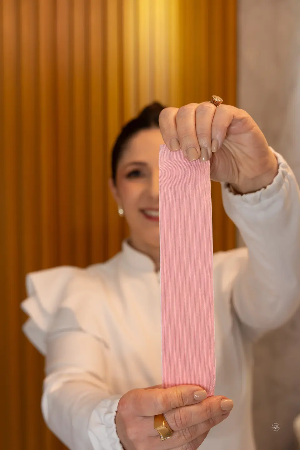 Faixa de taping rosa esticada entre as mãos da Flávia, em primeiro plano